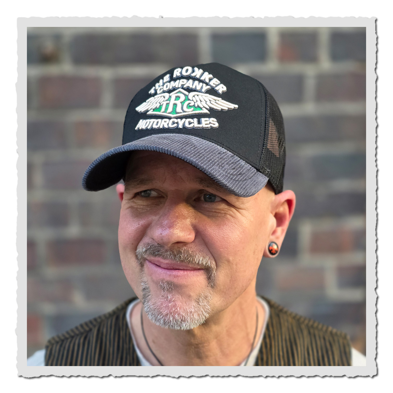 Rokker Cap Wings – Mann vor Ziegelwand trägt das schwarze Trucker Cap mit gesticktem Logo